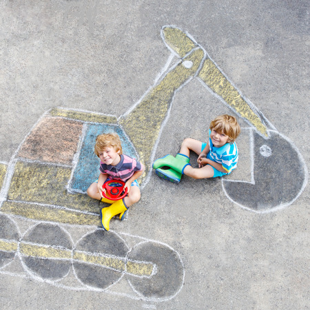 Two little happy kid boys having fun with excavator picture drawing with colorful chalk. の写真素材
