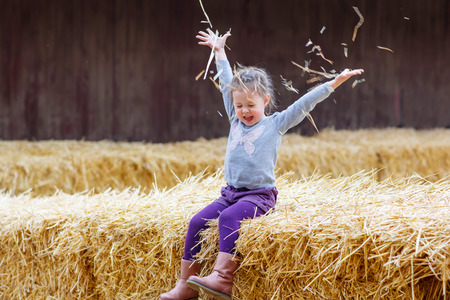 Funny little happy girl having fun with hay on a farm. Child enjoying autumn season and laughing. Happy childhood, lifestyle concept.の写真素材