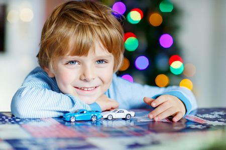 Adorable kid boy playing with cars and toys at home, indoor. funny child having fun with gifts. Colorful christmas lights on background. Family, holiday, kids lifestyle concept.の写真素材