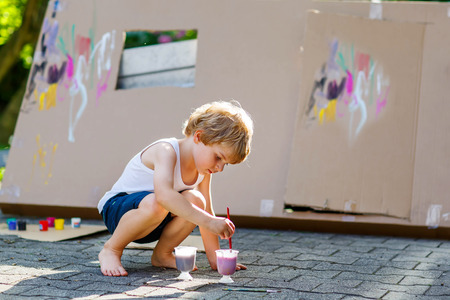Adorable little kid boy painting big paper house with colorful paintbox. Children having fun outdoors. Creative leisure, preschool project for pupil.の写真素材