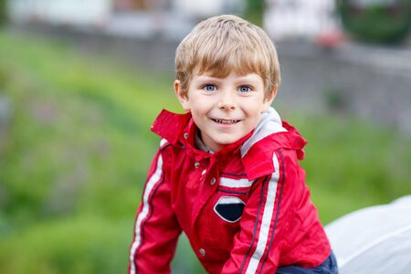 Portrait of little schoolboy outdoors on rainy day. Child having fun and wearing colorful waterproof clothesの写真素材
