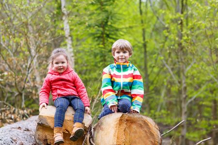 Two little cute smiling kids in bright jackets walking together in a forest on a rainy day. Friendship between siblings. Happy family conceptの写真素材
