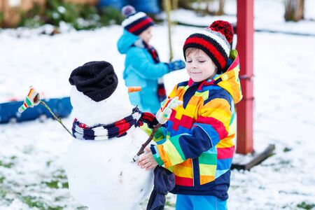 Two little siblings boys making a snowman, playing and having fun with snow, outdoors  on cold day. Active outdoors leisure with kids in winter.の写真素材