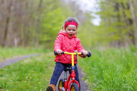 Happy funny kid girl and colorful raincoat riding his first bike on summer day. Active leisure for children outdoors.の写真素材
