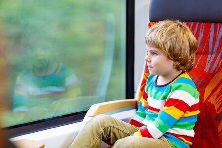 Beautiful little kid boy looking out train window outside, while it moving. Going on vacations and traveling by railway.の写真素材