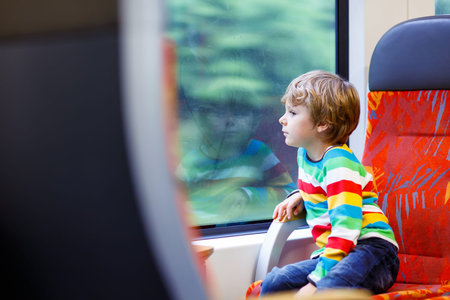 Lovely little kid boy looking out train window outside, while it moving. Child going on vacations...