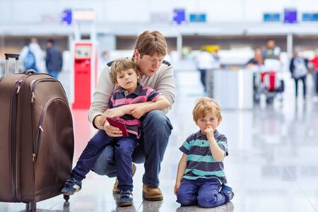 Tired father and two little sibling kids boys at the airport, traveling together. Upset family waiting. Canceled flight due to pilot strike.の写真素材
