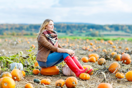 Beautiful young woman in red rain boots working on pumpkin farm or patch. Girl having fun with farming. Thanksgiving, harvest or halloween conceptの写真素材