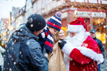 Little toddler boy with father on Christmas market. Funny happy kid taking gift from bag of Santa Claus. holidays, christmas, childhood and people conceptの写真素材