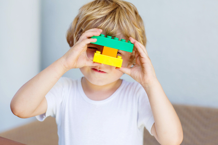 Adorable blond child playing with lots of colorful plastic blocks indoor. Active kid boy having fun with building and creating.の写真素材