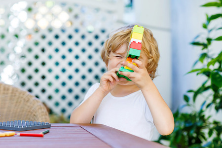 Funny happy blond child playing with lots of colorful plastic blocks indoor. Active kid boy having fun with building and creating.の写真素材