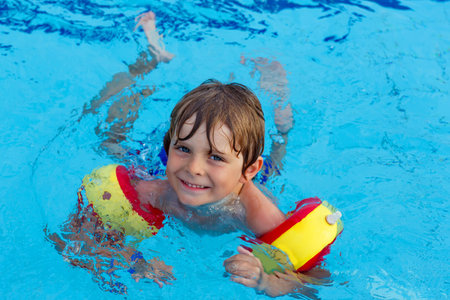 Happy little kid boy having fun in an swimming pool. Active happy child wearing safe swimmies....