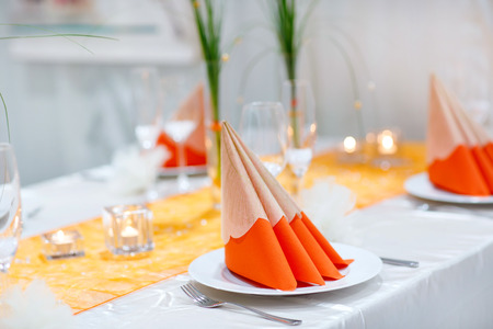 Table set  for wedding or event party. Elegant and luxury decoration in soft orange with flowers, silver cutlery, wine glasses, textile napkin.の写真素材