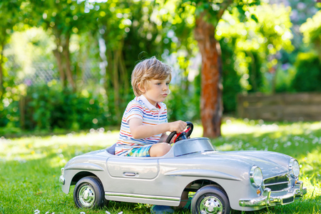 Adorable little preschool kid boy driving big toy old vintage car and having fun, outdoors. Active leisure with children during school holidays on warm summer sunny day.の写真素材
