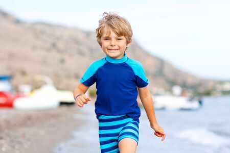 Happy little blond kid boy running on ocean beach. Child having fun. Vacations, summer, travel concept. Funny preschooler enjoying summer vacations on sea.の写真素材