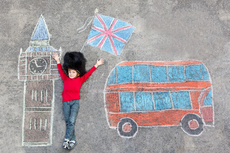 Happy little kid boy in british queen's guard soldier uniform having fun with London picture drawing with colorful chalks. With Big Ben, Union Jack and red bus.の写真素材