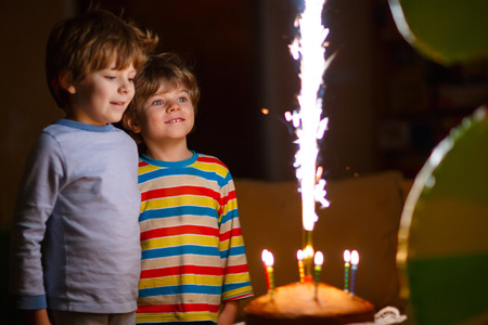 Beautiful kids, little boys celebrating birthday and blowing candles on homemade baked cake, indoor. Birthday party for children. Happy twins about fireworksの写真素材