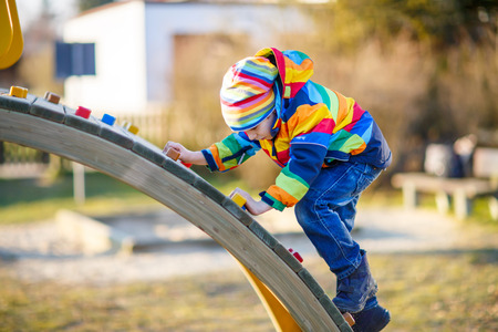 Adorable kid boy having fun on outdoor playground. child climbing on scaffolding on warm sunny spring or autumn day. Active leisure with kids. Boy wearing colorful clothesの写真素材