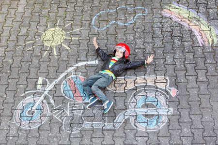 Creative leisure for children: Happy little child of four years in helmet having fun with motorcycle picture drawing with colorful chalks. Children, lifestyle, fun concept.の写真素材