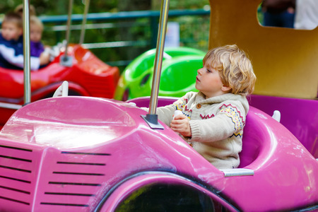 Funny little kid boy riding on car on roundabout carousel in amusement park. Happy toddler having fun outdoors on sunny day.の写真素材