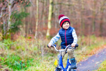 Happy kid boy of 3 years having fun in autumn forest with a bicycle on beautiful fall day. Active child making sports. Safety, sports, leisure with kids concept.の写真素材