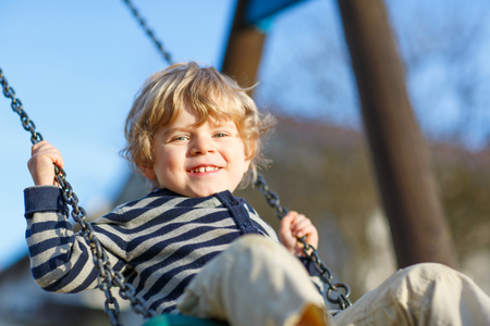 Little kid boy having fun and swinging on outdoor playground. Happy smiling child enjoying summer time. Carefree childhood concept.の写真素材