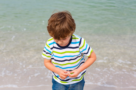 Adorable active little kid boy having fun on Naples beach, Florida. Happy cute child collecting shells.の写真素材