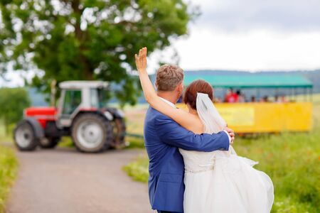 Happy wedding couple in pink poppy field. Beautiful bride in white dress and groom kissing and having fun in flower field on summer day. Just married, young family.の写真素材
