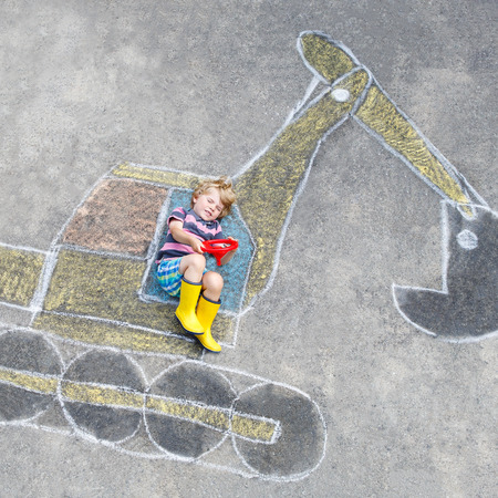 Happy funny little kid boy having fun with excavator picture drawing with colorful chalk. Creative leisure for children outdoors in summer.の写真素材