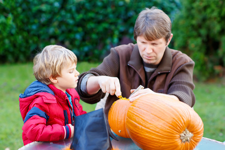 Young dad and his little kid boy making jack-o-lantern for halloween pumpkin in autumn garden, outdoors. Father and child, Family having fun togetherの写真素材