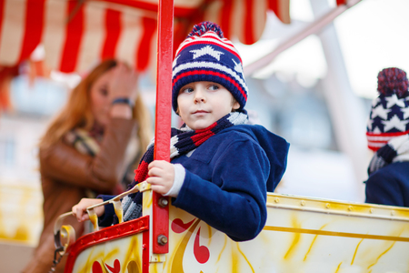 Adorable little kid boy on a carousel, ferris wheel at Christmas funfair or market. Mother and sibling on background. Happy child having fun.の写真素材