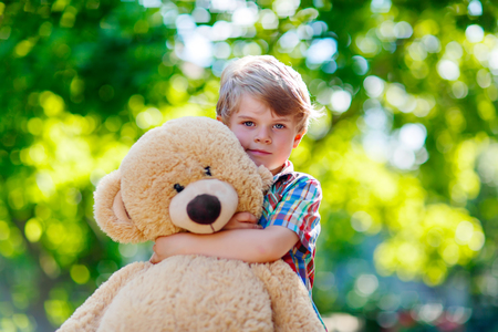 Little preschool kid boy playing with his big plush toy bear, outdoors. Child enjoying warm summer day in nature landscapeの写真素材