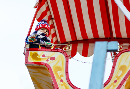Adorable little kid boy on a carousel, ferris wheel at Christmas funfair or market, outdoors. Happy child having fun. Holiday, children, lifestyle concept.の写真素材