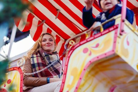 Young woman and little kid boy on a carousel, ferris wheel at Christmas funfair or market. Mother and son on background. Happy child having fun.の写真素材