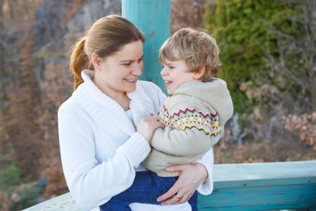 Mother and little son in park or forest, outdoors. Hugging and having fun together.