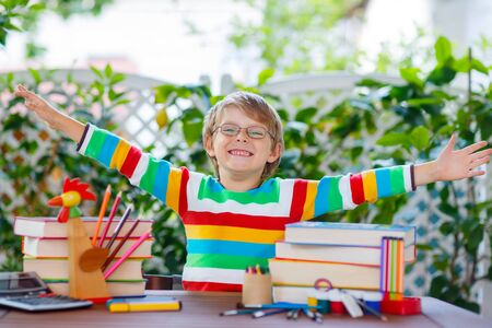 Cute beautiful little kid boy with glasses and lots of pupil's stuff like crayons pens, scissors and books. Child and student is back to school and happy about begin of lessons.の写真素材