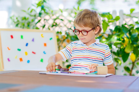 Funny adorable little kid boy with glasses holding wax crayons pens. Happy child and student is back...