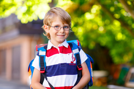Happy little kid boy with glasses and backpack or satchel on his first day to school or nursery. Child outdoors on warm sunny day, Back to school conceptの写真素材
