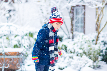 Winter portrait of little kid boy in colorful clothes, outdoors during snowfall. Active outdoors leisure with children in winter on cold snowy days. Happy child having fun with snowの写真素材