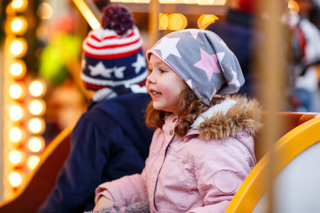 Adorable little boy and girl, siblings on a carousel at Christmas funfair or market, outdoors. Happy children, friends having fun. Selective focus on one child. Holiday, children, lifestyle concept.の写真素材
