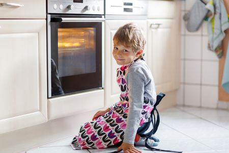 Cute funny blond kid boy baking muffins in domestic kitchen. Child having fun with helping, sitting near ofen and waiting for cupcakes.の写真素材