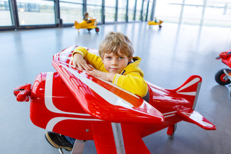 Adorable little preschool kid boy driving big toy old vintage pedal plane and having fun, indoors. Active leisure with children during school holidaysの写真素材