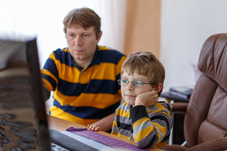 Middle-aged father and little kid boy learning and making school homework on computer. Family, dad and son using software on pc device. Education concept.の写真素材