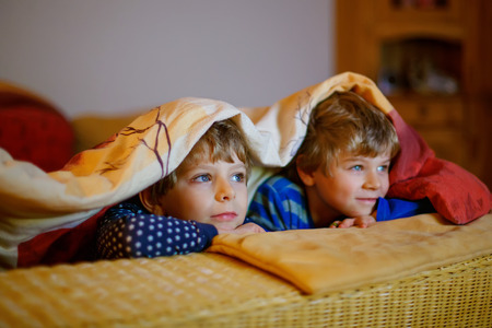 Happy little brothers, adorable kid boys watching television while lying. Funny children enjoying cartoonsの写真素材