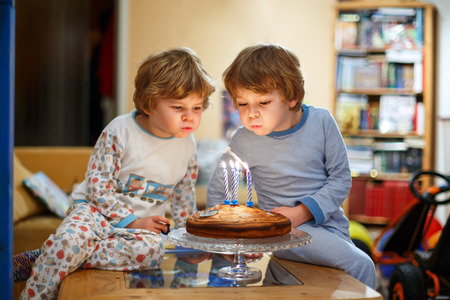 Beautiful kids, little boys celebrating birthday and blowing candles on homemade baked cake, indoor. Birthday party for siblings hildren. Happy twins about giftsの写真素材