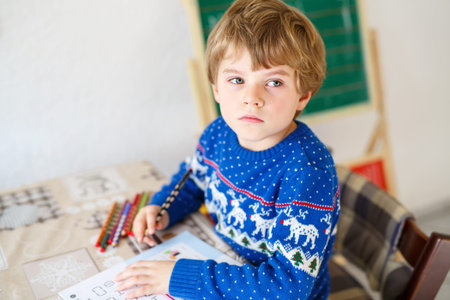 Portrait of frustrated sad school kid boy at home making homework. Little child writing with...
