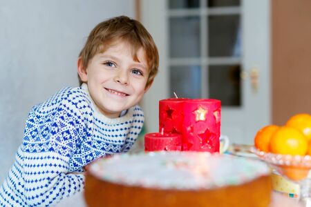 Beautiful little kid boy standing by festive table at Christmas time and holding candle. Excited child celebrating traditional . Xmas party. Catholic and christian celebration in Europe and USAの写真素材
