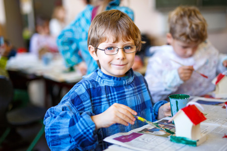 Little school kid boy with glasses coloring bird house with watercolors in labor classroom. child having fun with learning, building skills, education. Primary school and pupil.の写真素材