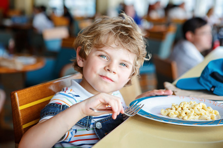 Cute healthy preschool boy eats pasta sitting in school canteenの写真素材