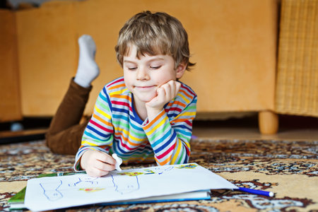 preschool kid boy at home making homework, painting a story with colorful pens